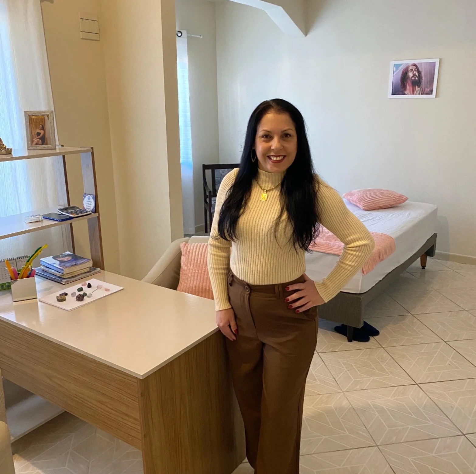 Janaina Amorim em seu consultório, com mesa de atendimento, pedras e cama de tratamento